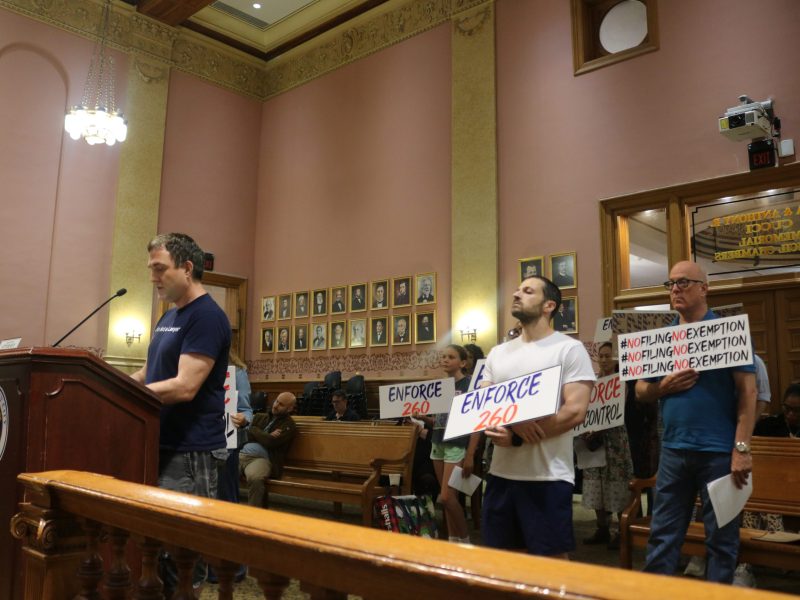 Person stands at podium while two others stand behind them holding the signs.