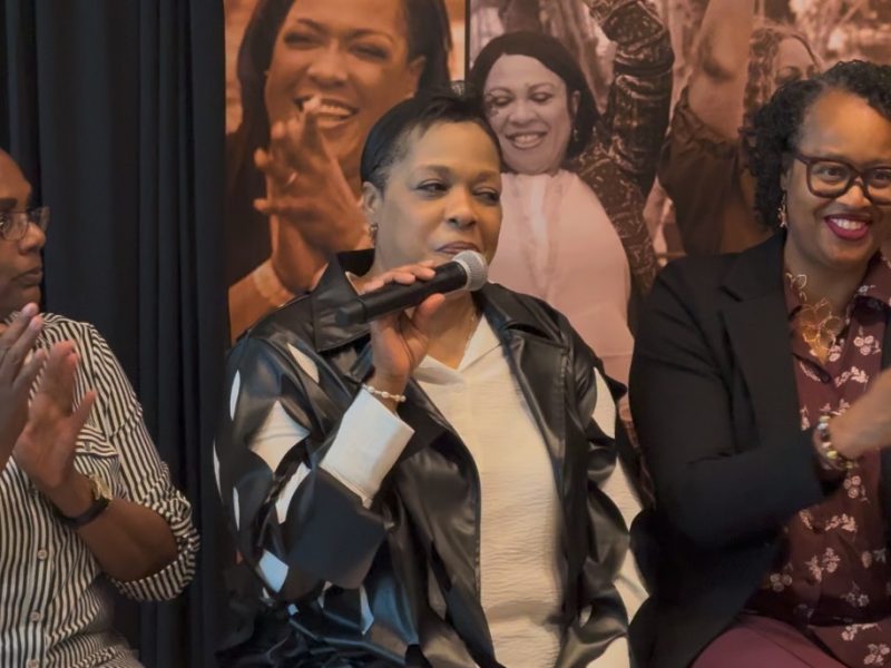 Three women sitting, one holds mic