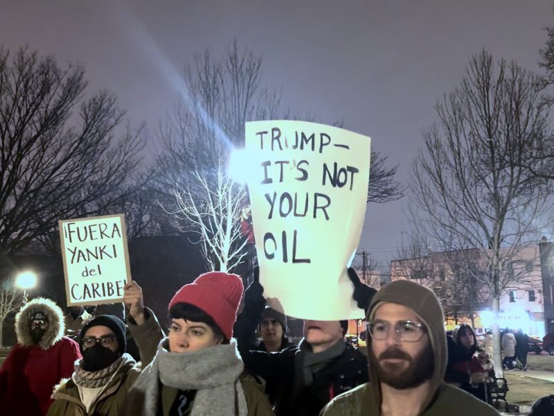 People gather holding signs at night. sign says trump it's not your oil