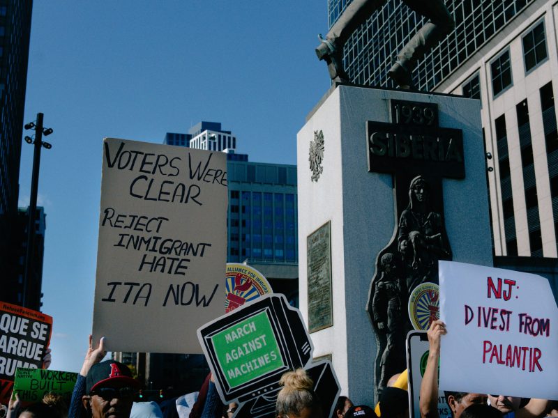 People holding signs that say "voters were clear reject immigrant hate ITA now" And "NJ Divest from palantir"