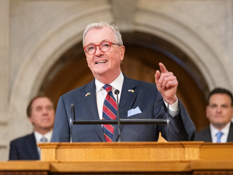 Phil murphy stands at podium pointing while craig coughlin and nick scutari sit behind him