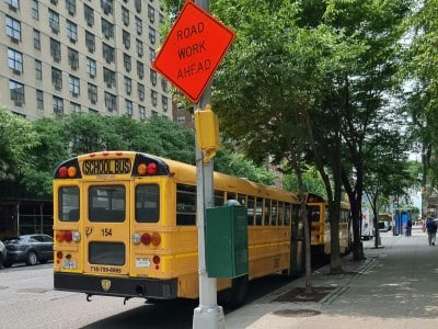 Yellow school buses parked on a city street in New York with road work signs in summer.