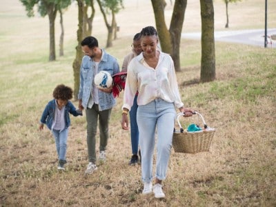 A joyful family walking in a park, carrying a picnic basket and a ball on a sunny day.
